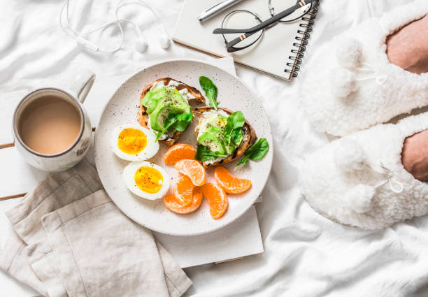 istock Breakfast in bed. Coffee, avocado sandwiches, boiled egg and tangerine on a light background, top view. Morning inspiration 1089046470