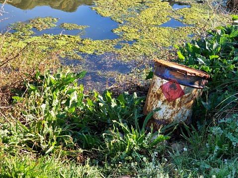 A chemical drum or container on the edge of a river bank