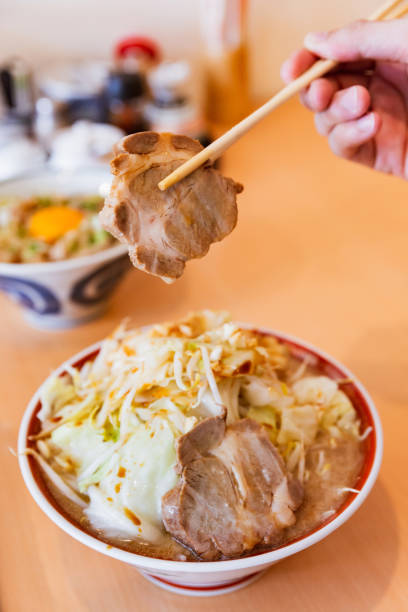 istock A hand holding Chashu by chopsticks from Tonkotsu chashu ramen topping with cabbage, bean sprout and garlic served in oversized portion. 1089087950