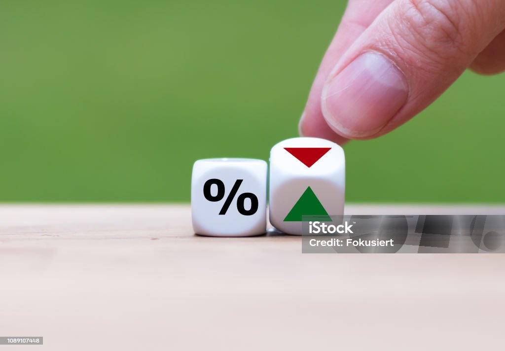 Hand is turning a dice and changes the direction of an arrow symbolizing that the interest rates are going down (or vice versa) Interest Rate Stock Photo