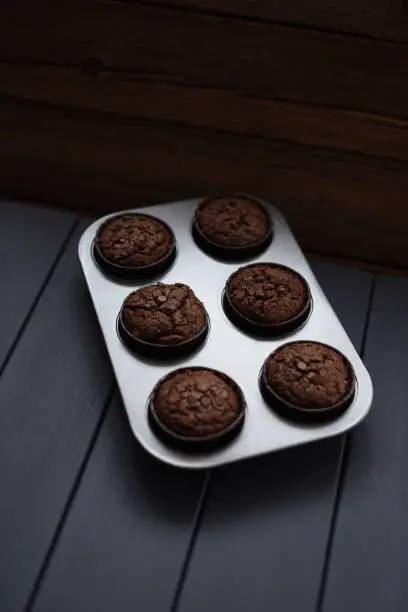 Minimalist style homemade pastry. Chocolate muffins with chocolate chips in metal baking tray on dark background copyspace