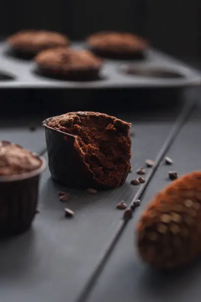 Hygge cozy dessert. Half eaten tasty chocolate muffins with small chocolate chips on dark background vertical