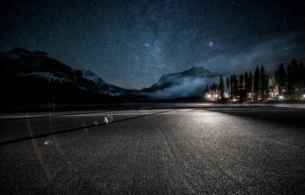 empty tarmac road under milky way by Emerald Lake in Yoho national park empty tarmac road under milky way by Emerald Lake in Yoho national park,British Columbia, Canada. dark road stock pictures, royalty-free photos & images