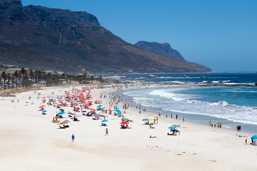 Beach goers relaxing in the shade of umbrellas on a hot summer afternoon in Cape Town, Camps Bay Beach, South Africa.