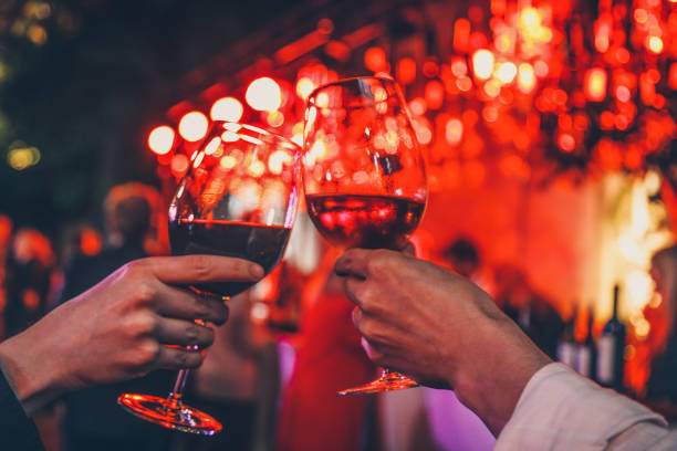 Couple toasting wine glasses Detail of two hands cheering with glasses of  red wine on dinner date for two. Romantic lights background. Love and food concept glasses in vibe plant garden date night romance stock pictures, royalty-free photos & images