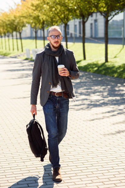 istock Young businessman with backpack drinks coffee during lunch break near modern office center outdoors. 1089144180