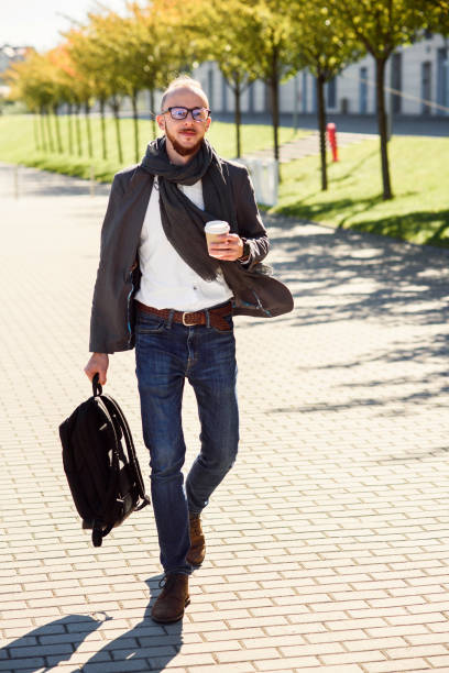 istock Young businessman with backpack drinks coffee during lunch break near modern office center outdoors. 1089144340