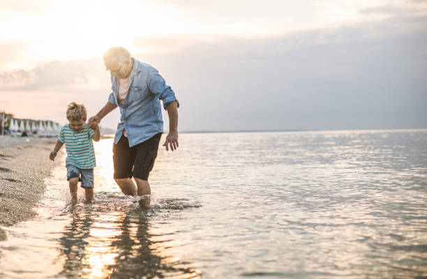 Grandfather and grandson at the beach Grandfather and grandson walking at the beach on sunset grandson photos stock pictures, royalty-free photos & images