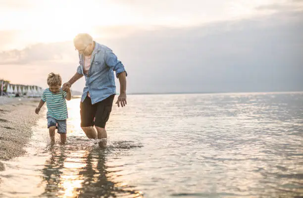 Grandfather and grandson walking at the beach on sunset