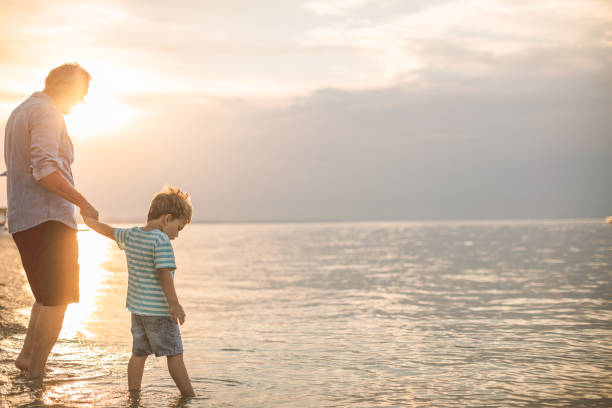 Grandfather and grandson walking at the beach on sunset