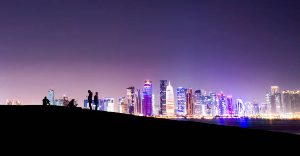 Silhouette of some people relaxing on a hill with the beautiful Doha skyline in the background. Doha, Qatar. Silhouette of some people relaxing on a hill with the beautiful Doha skyline in the background. Doha, Qatar. business architecture blue people stock pictures, royalty-free photos & images