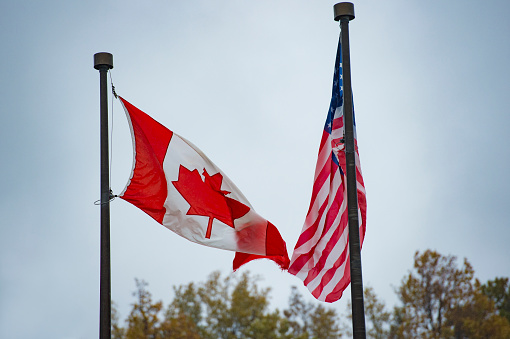 Close-up view of an American flag and a Canadian flag waving in the wind.