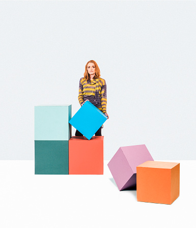 Woman in a white room stacking blocks or boxes. Concept could be moving or new beginning. Image has copy space and room for creativity.