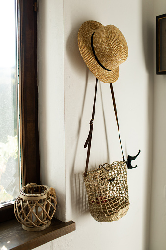 wicker hat and bag hang on a white wall in the hallway at home