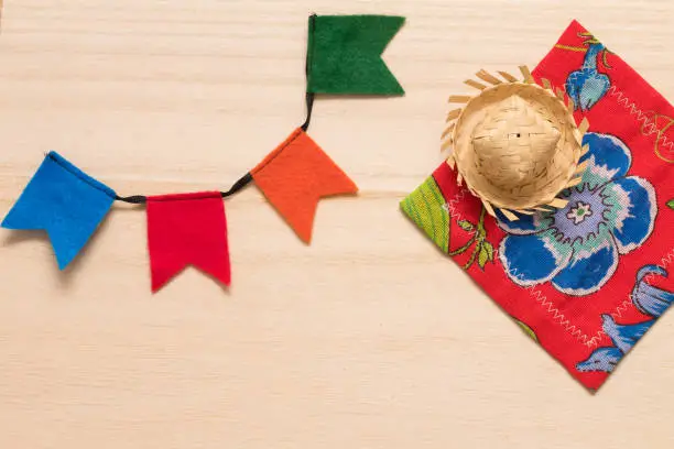 Traditional party supplies for the typical brazilian festival "Festa Junina" (June Festival) background. Cute handmade colorful flags, tiny hat and citra fabric (brazilian "Chita" fabric) on wooden background. Handmande felt items