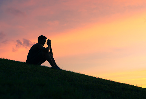 Silhouette of man praying at sunset.