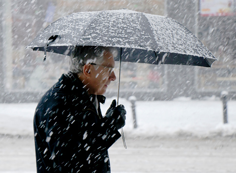 Belgrade, Serbia - December 15, 2018: Elderly man walking alone under umbrella snowy city street in heavy snowfall