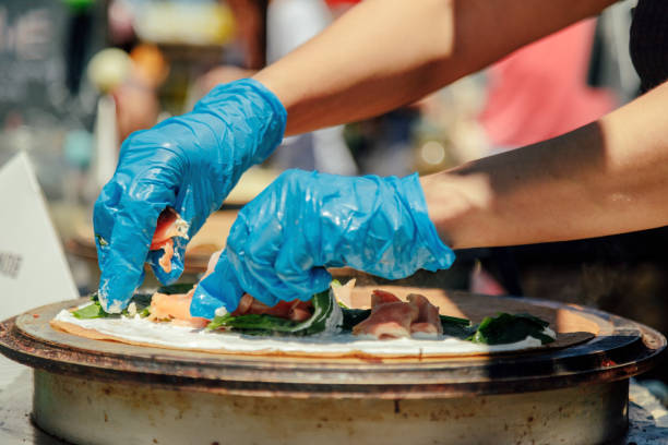 Cook's hand putting ham on a crepe while cooking next to others
