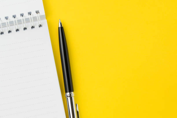 istock Top view of black pen with clean white notebook open with copy space on solid yellow table background for presentation, writer or school education, blogger, novel and friction or brand story concept 1089184390
