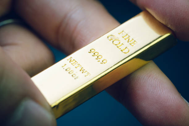 Hand holding gold bar as investment asset or safe haven on financial crisis, shinny ingot or bullion studio shot with dark background stock photo