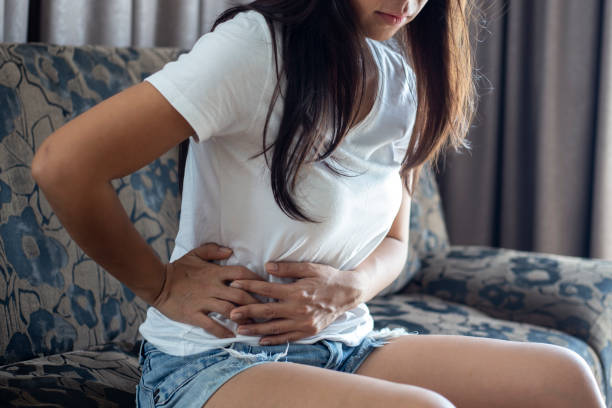 asian woman suffering from abdominal pain while sitting at home - ovulação imagens e fotografias de stock