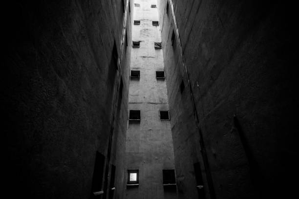 Small bathroom windows in an air vent pit inside a tall communist era block of flats, in Bucharest, Romania (black and white).