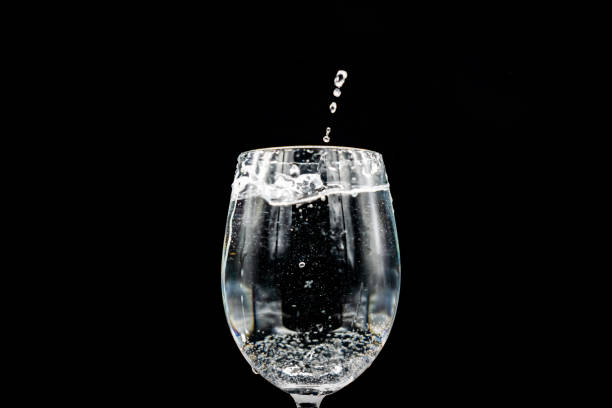 A glass filled with water, shades of blue, white bokeh from lights in the background, small light sources.