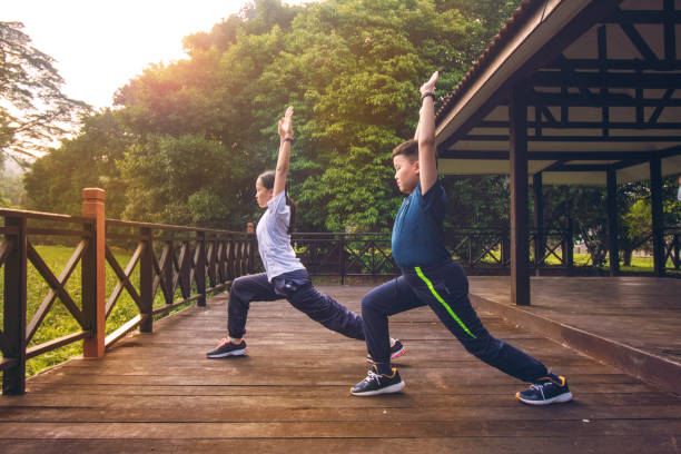 young asian athletic brother and sister doing exercise stretching and practicing yoga warrior pose in nature outdoor park morning. wearing sports outfit. concept of Healthy lifestyle, training workout asian, children, sibling, family, malaysia, chinese, sportswear, Exercising, Sport, Stretching, yoga warrior position stock pictures, royalty-free photos & images