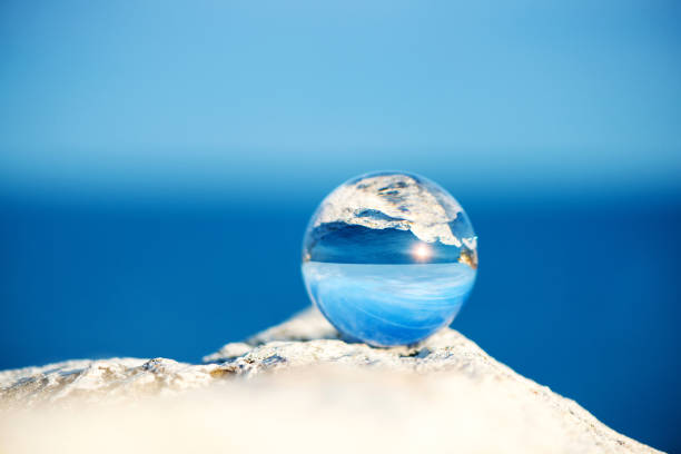 Upside down seascape with blue sky and overgrown with moss rocks - reflection in a lens ball - selective focus, space for text