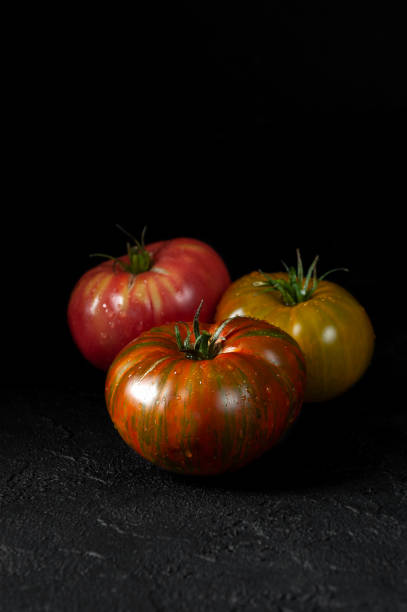tomates hereditarias. tres tomates de diferentes colores en un primer plano del fondo texturado negro. - heirloom tomato tomato vegetable fruit fotografías e imágenes de stock