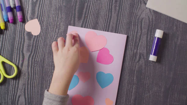 Girl's hands glueing a card. Valentine's Day Top view. Close up girl's hands glueing a card. Valentine's Day. happy valentines day book stock pictures, royalty-free photos & images