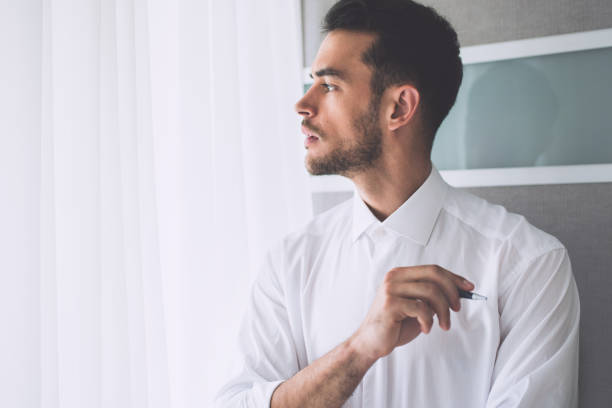istock Thinking businessman on white shirt with a pen look at one side. Office grey background. 1089294768