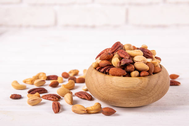 Different kinds of organic nuts in wooden bowl. Mixed nuts in wooden bowl and scattered on table. Trail mix of pecan, almond, macadamia & brazil edible nuts with walnut hazelnut on wood textured surface. Background, copy space, top view, close up. nut variation healthy lifestyle pistachio stock pictures, royalty-free photos & images