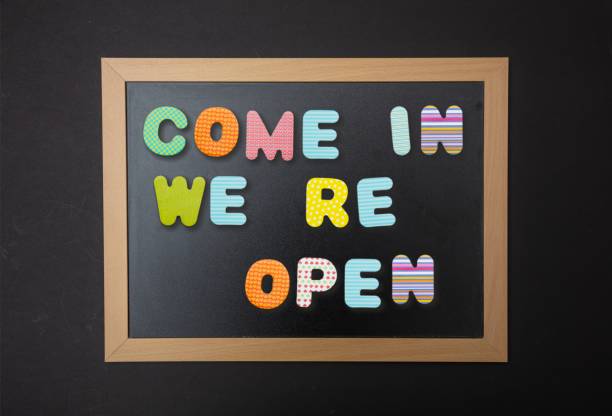 istock Board with black frame, text Come in, we re open in colorful letters, black wall background 1089299236