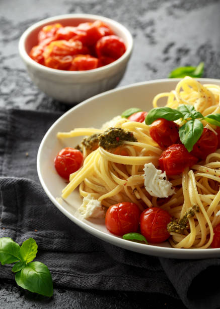 istock Pasta with green pesto sauce, roasted cherry tomatoes and mozzarella cheese in white plate on dark rustic background 1089307724
