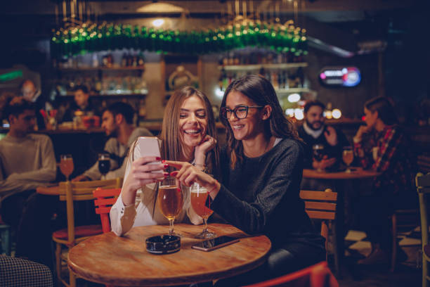 Girlfriends sitting in pub Group of people, sitting in pub drinking beer and talking. friends in bar with phones stock pictures, royalty-free photos & images