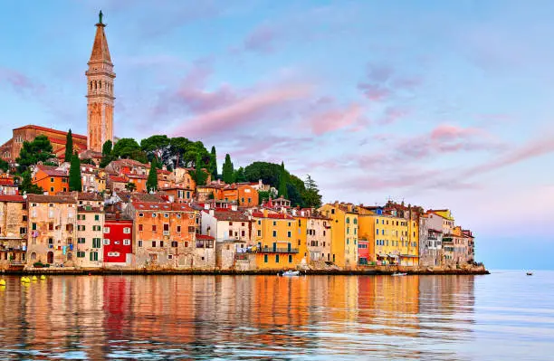 Rovinj Croatia. Sunrise sky above vintage town at Istria peninsula in Adriatic Sea. View from water at old Mediterranean architecture buildings. Coastline and tower of Church of Saint Euphemia.