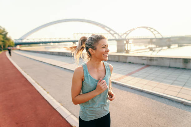 lächelnd weibliche läufer mit blonden haaren und pferdeschwanz, gekleidet in sportbekleidung auf den kay in den frühen morgenstunden im sommer ausgeführt. - running track women running spring stock-fotos und bilder