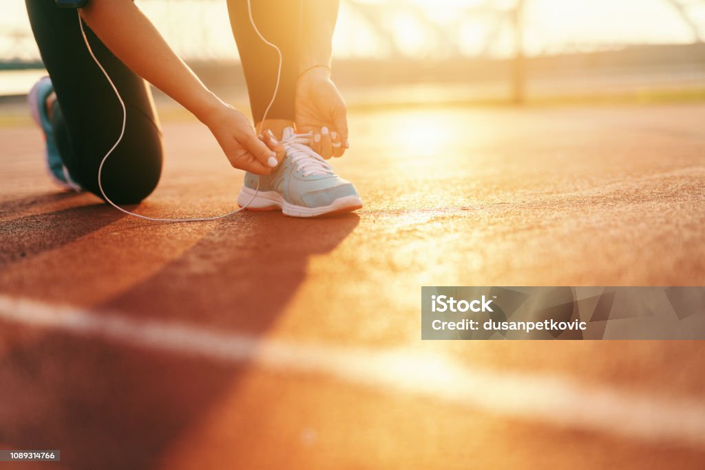 Close up of sporty woman tying shoelace while kneeling on the court early in the morning. Active Lifestyle Stock Photo