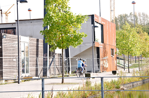 Tourists biking past a part of Hochofenplatz - a decommissioned steel factory - and an old building with graffiti-covered brick wall in Phoenix West, Dortmund - Germany