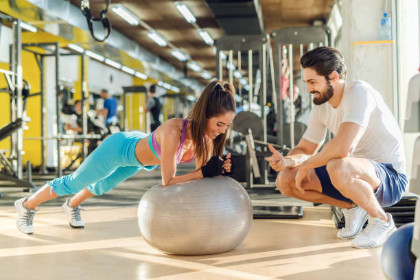 sporty smiling woman doing planks on pilates ball while her personal trainer crouching next to her and cheering for her. - secrecy instructor exercising individuality imagens e fotografias de stock