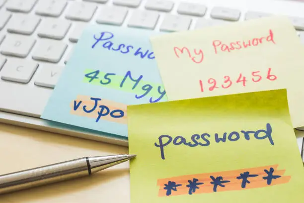 Silver pen pointing at handwriting passwords with highlight colors written on paper notes at modern white keyboard with office table on background. Data privacy management and cyber security concepts.