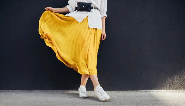 Photo of Cropped body shot of attractive woman in beautiful yellow skirt. Caucasian female fashion model standing over gray wall background outdoor with copy space.