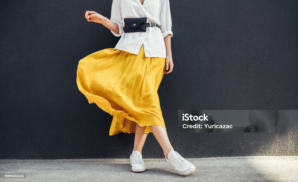 Horizontal abgeschnitten Bild stilvoll schlanken Frau in schönen gelben Rock. Kaukasische weibliche Mode Modell über graue Wand Hintergrund mit textfreiraum im Freien stehen. - Lizenzfrei Mode Stock-Foto