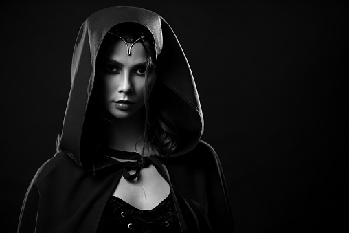 Black and white portrait of gorgeous beautiful girl in road clothes wearing hood on. Close up of elegant woman in cloak tied around neck mysteriously looking at camera. Black and white isolated.