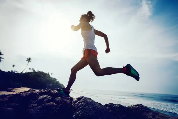 Photo of Young fitness woman trail runner running to rocky mountain top on seaside