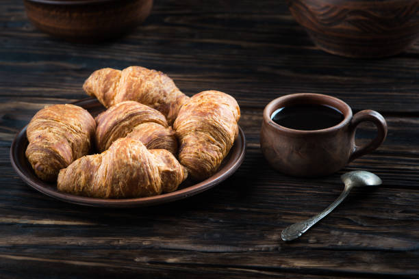 チョコレート クロワッサンは、粘土板、その隣にはスプーンと一杯のコーヒー - breakfast bread table drop ストックフォトと画像