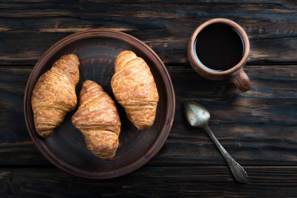 チョコレート クロワッサンは、粘土板、その隣にはスプーンと一杯のコーヒー - breakfast bread table drop ストックフォトと画像