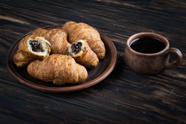 チョコレート クロワッサンは、粘土板、その隣にはスプーンと一杯のコーヒー - breakfast bread table drop ストックフォトと画像