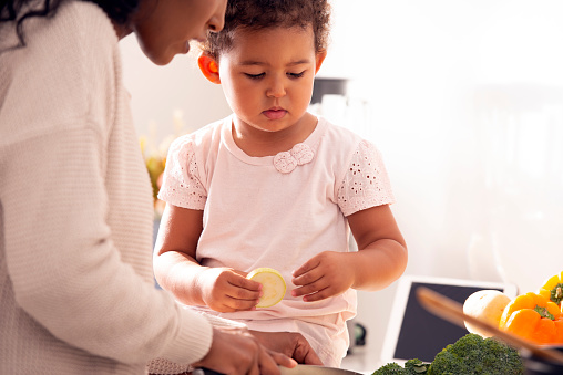 Close up image of a girl holding a slice of zucchini, helping a mother to cook in the kitchen.